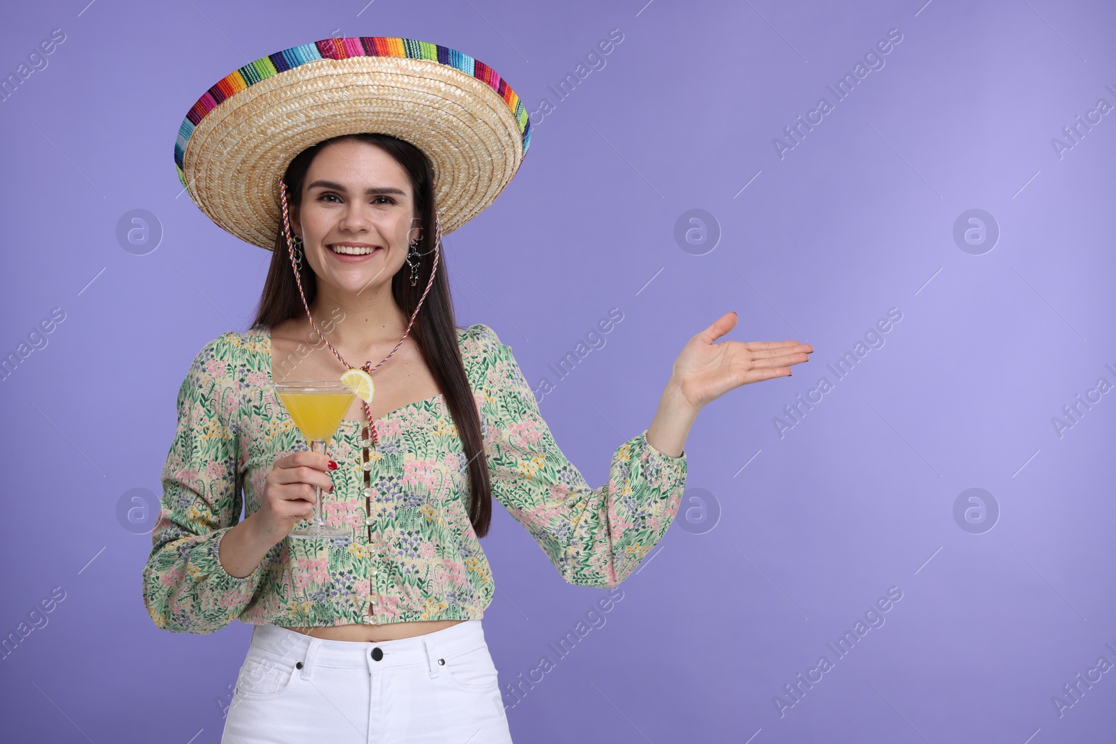 Photo of Young woman in Mexican sombrero hat with cocktail on violet background. Space for text