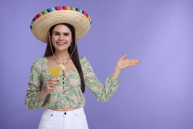 Young woman in Mexican sombrero hat with cocktail on violet background. Space for text