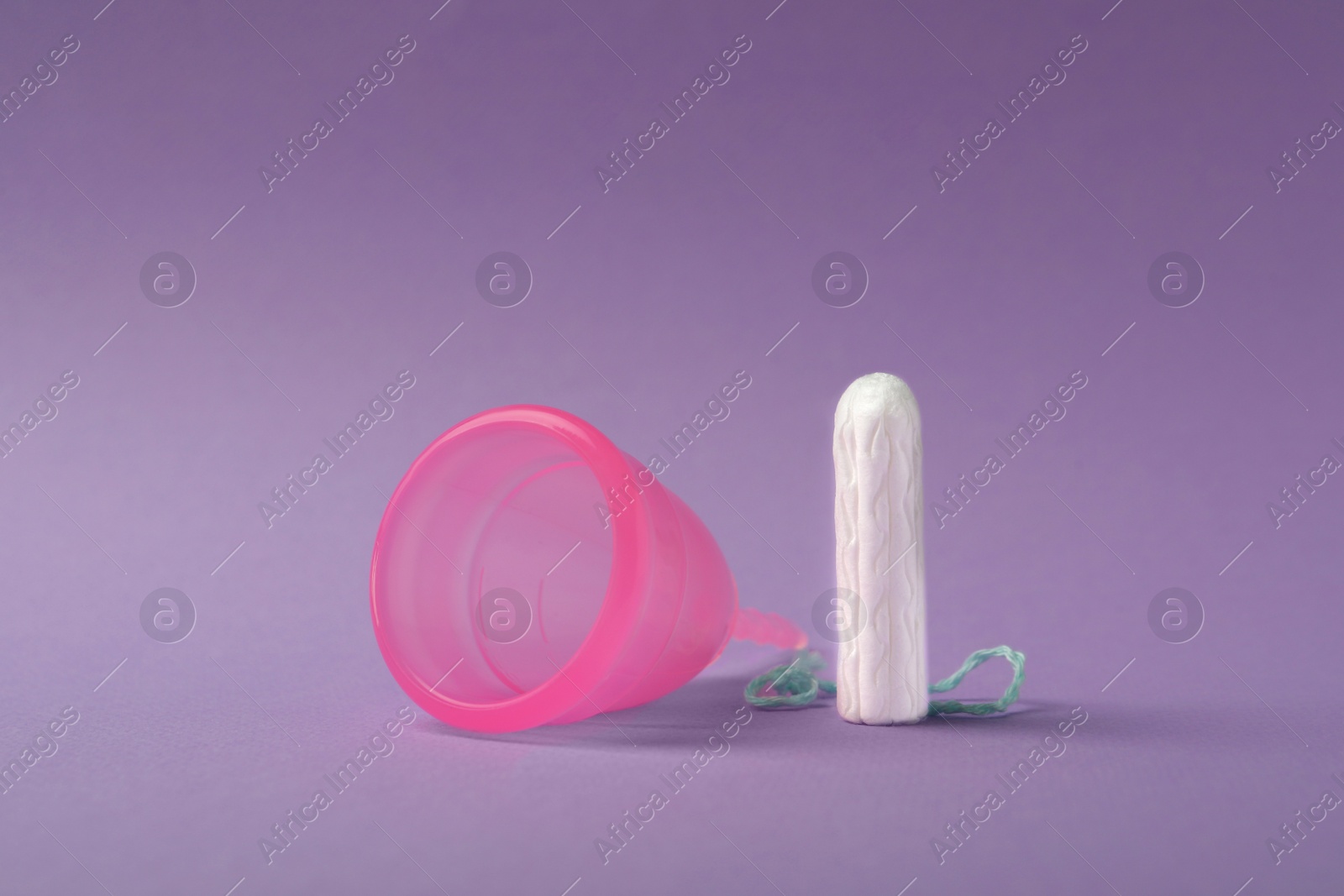 Photo of Menstrual cup and tampon on violet background