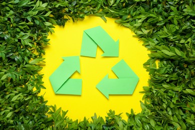 Photo of Recycling symbol and branches of green plant on yellow background, flat lay
