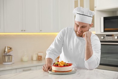 Happy professional confectioner with delicious cake at table in kitchen