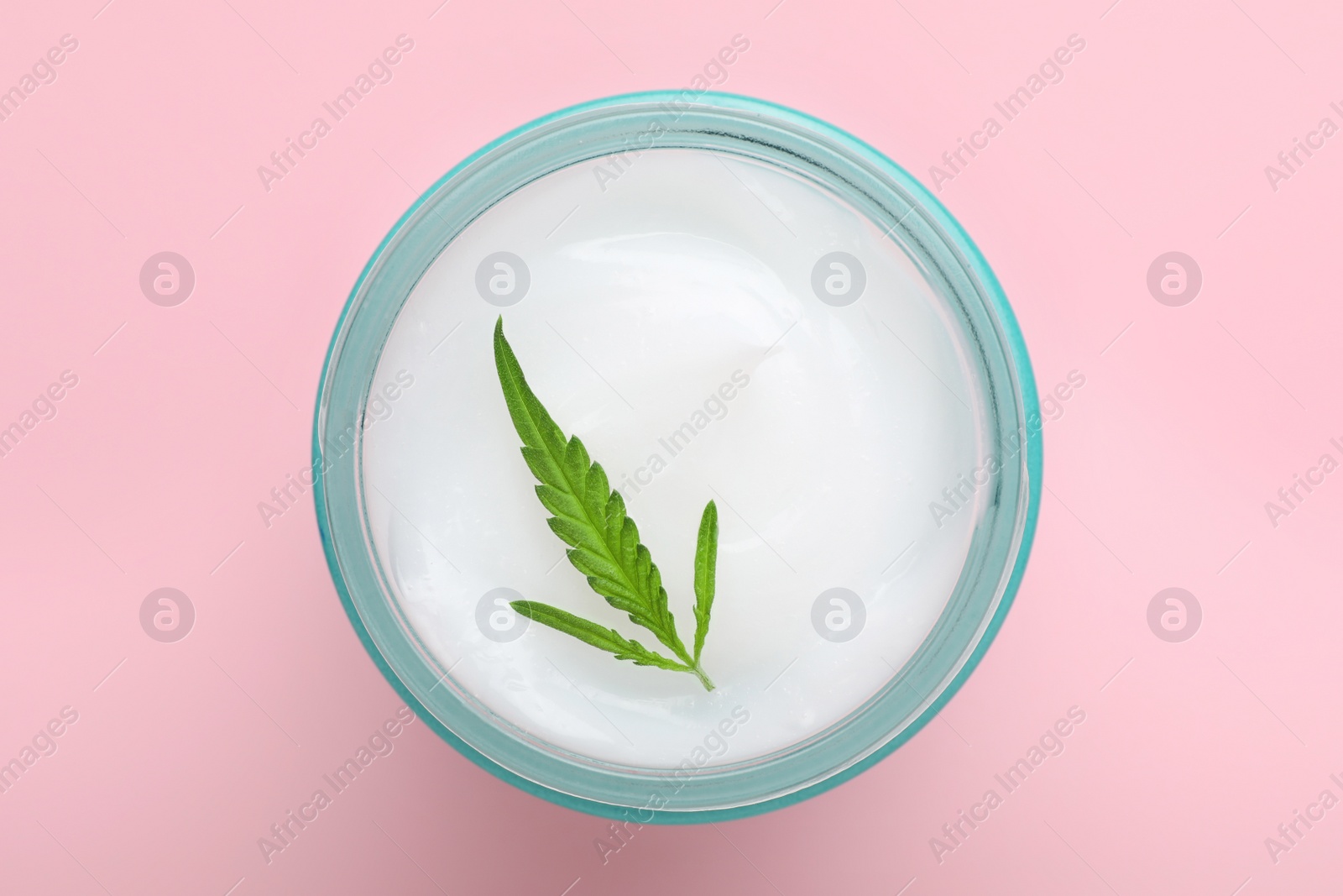 Photo of Jar of hemp cream with green leaf on pink background, top view. Natural cosmetics