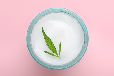 Photo of Jar of hemp cream with green leaf on pink background, top view. Natural cosmetics