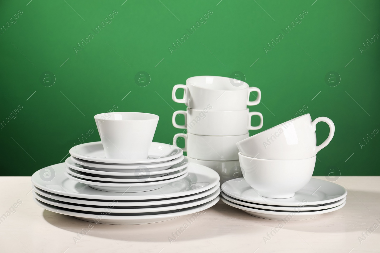 Photo of Set of clean dishware on white table against green background