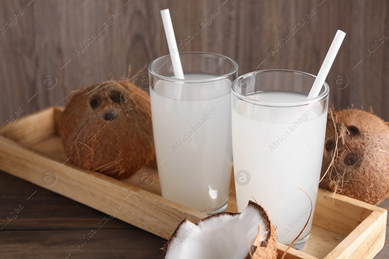 Photo of Glasses of coconut water with straws and nuts on wooden table