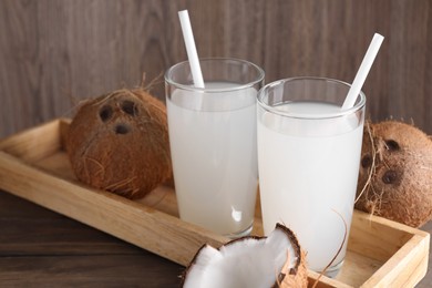 Photo of Glasses of coconut water with straws and nuts on wooden table