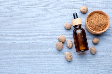 Photo of Bottle of nutmeg oil, nuts and powder on grey wooden table, flat lay. Space for text