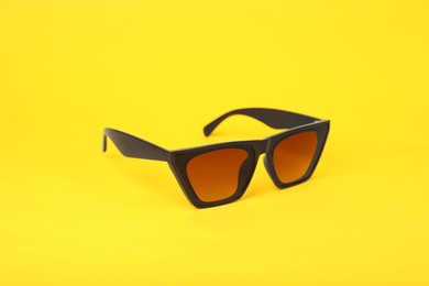 Photo of Stylish pair of sunglasses on yellow background