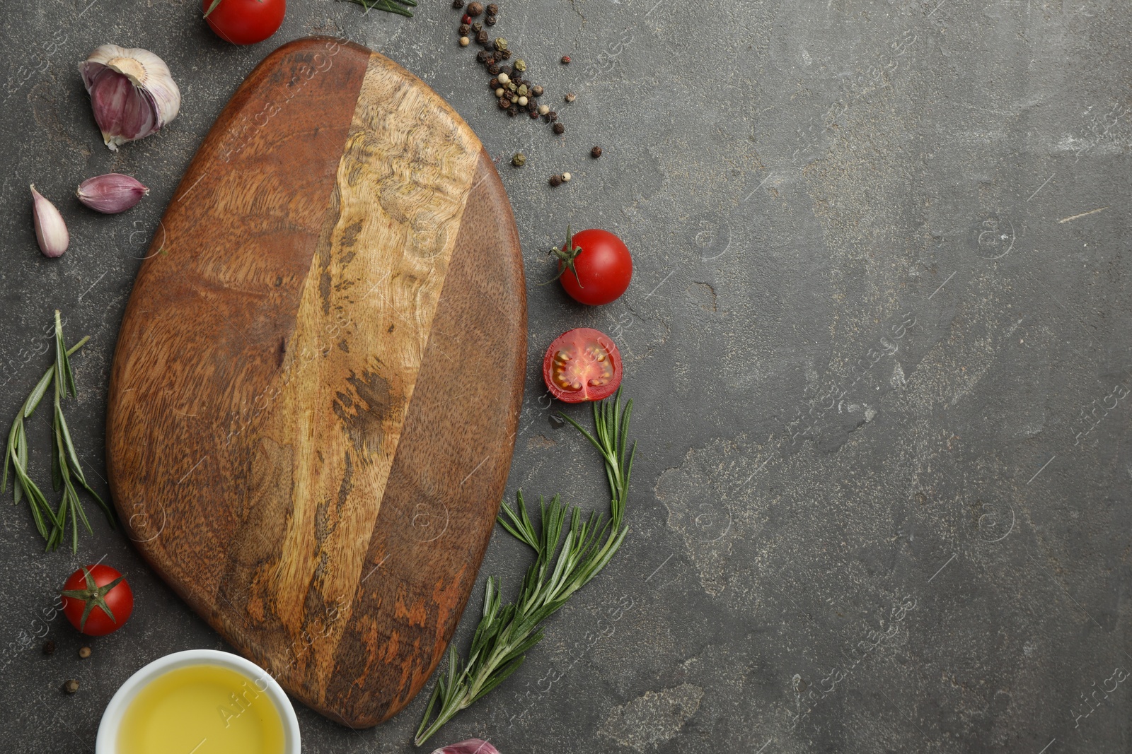 Photo of Cutting board, rosemary, garlic, oil and tomatoes on black table, flat lay. Space for text