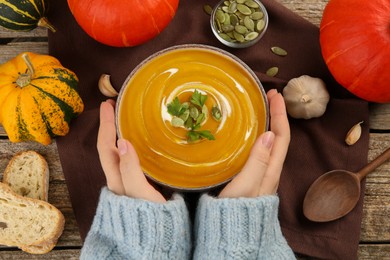 Woman with bowl of delicious pumpkin soup at table, top view