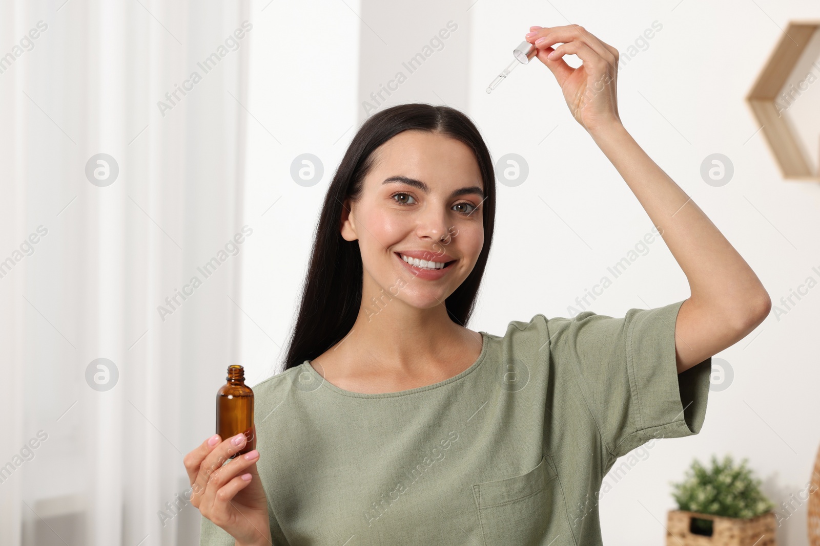 Photo of Beautiful woman applying hair serum in room. Cosmetic product