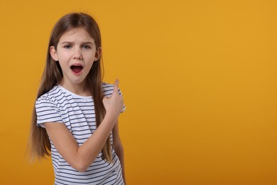 Photo of Surprised girl pointing at something on yellow background. Space for text