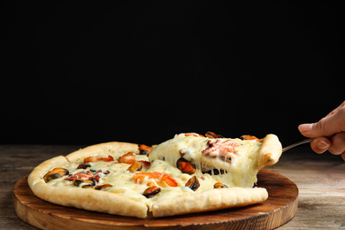 Photo of Woman taking piece of delicious seafood pizza at wooden table, closeup