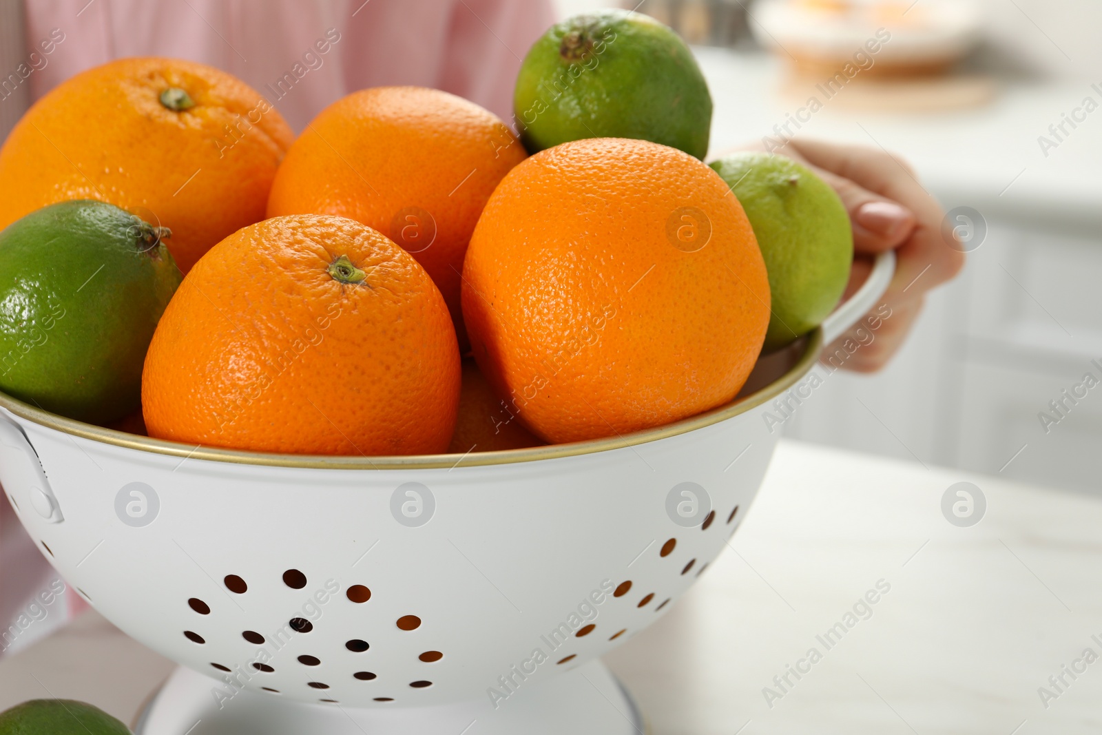 Photo of Woman holding colander with fresh fruits at white marble table, closeup