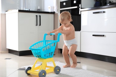 Cute baby with toy walker in kitchen. Learning to walk