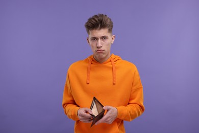 Upset man with empty wallet on purple background