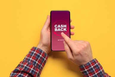 Image of Man using smartphone with word Cashback on orange background, top view