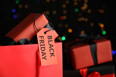Photo of Gift box with Black Friday tag against blurred lights, closeup