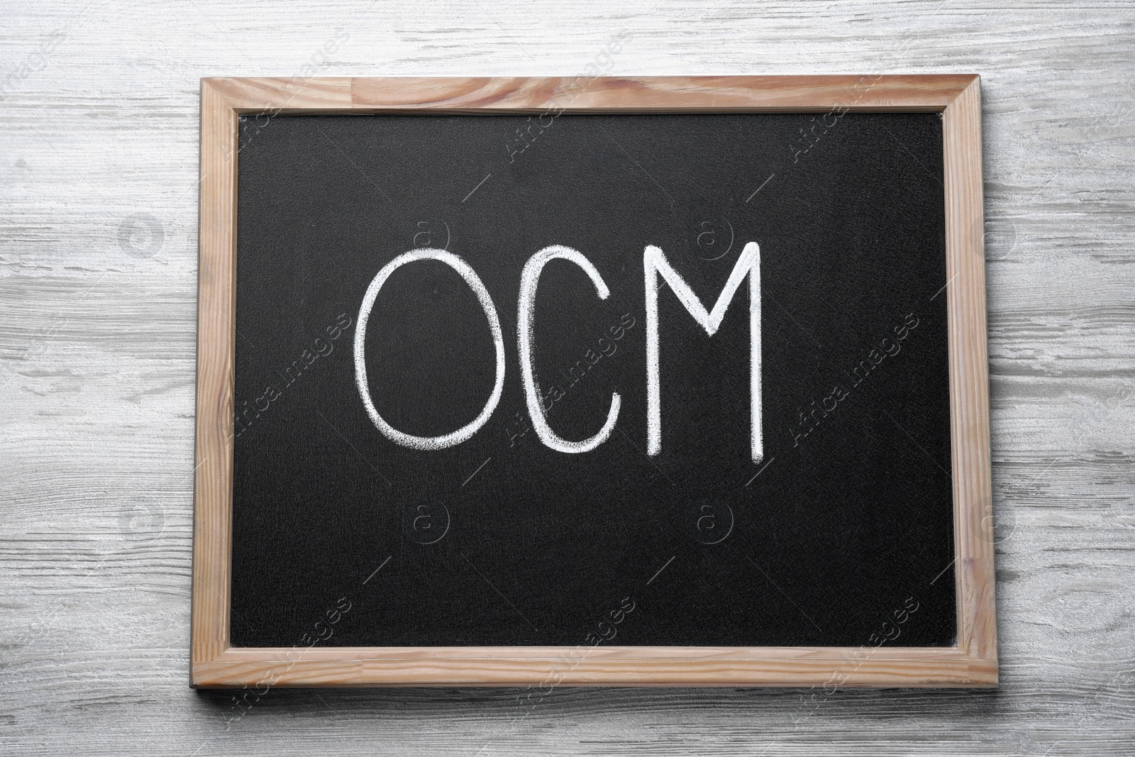 Photo of Small blackboard with abbreviation OCM (Organizational Change Management) on white wooden background, top view