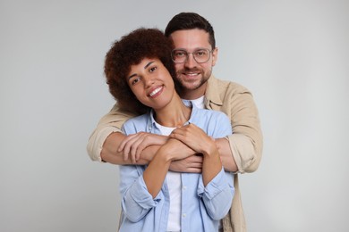 International dating. Happy couple hugging on light grey background