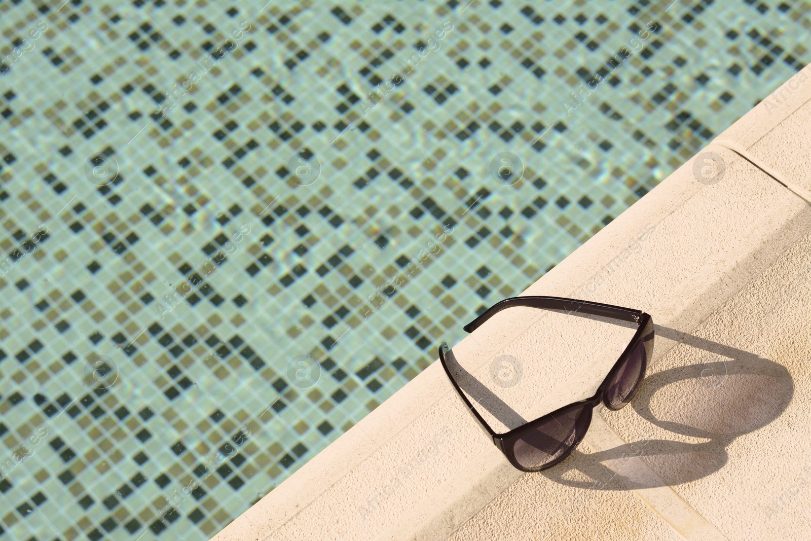 Photo of Stylish sunglasses near outdoor swimming pool on sunny day, above view. Space for text