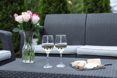 Photo of Vase with roses, glasses of wine and food on rattan table on outdoor terrace