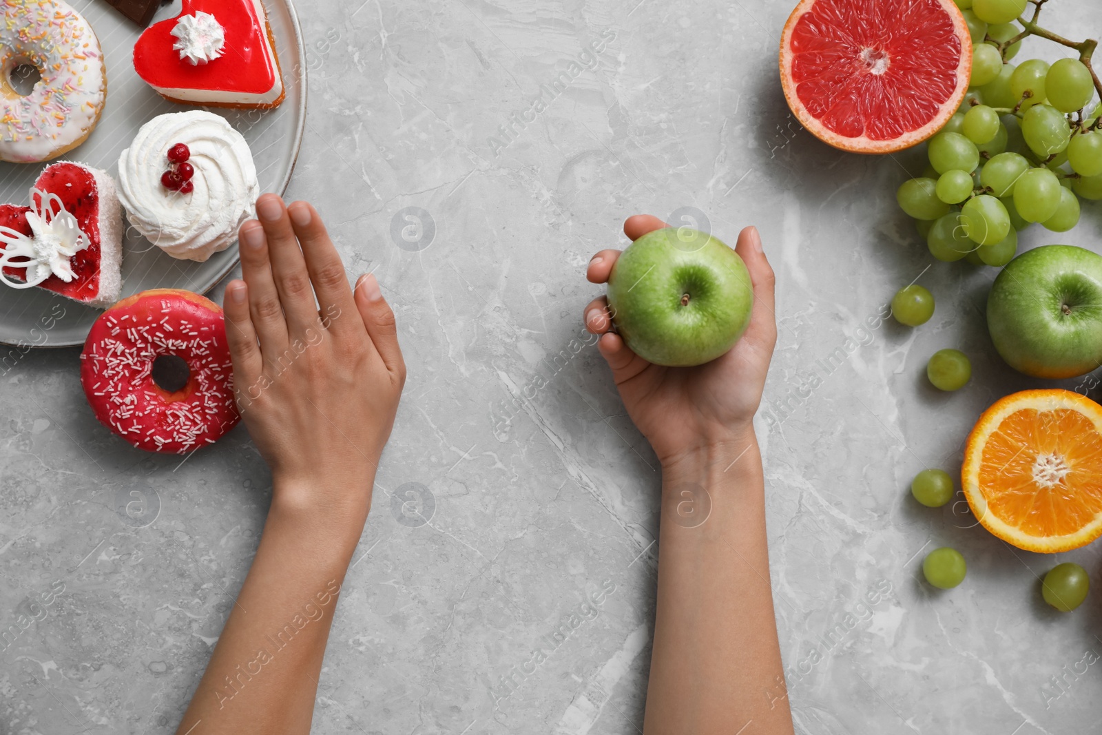 Photo of Concept of choice. Top view of woman holding apple at grey table, closeup