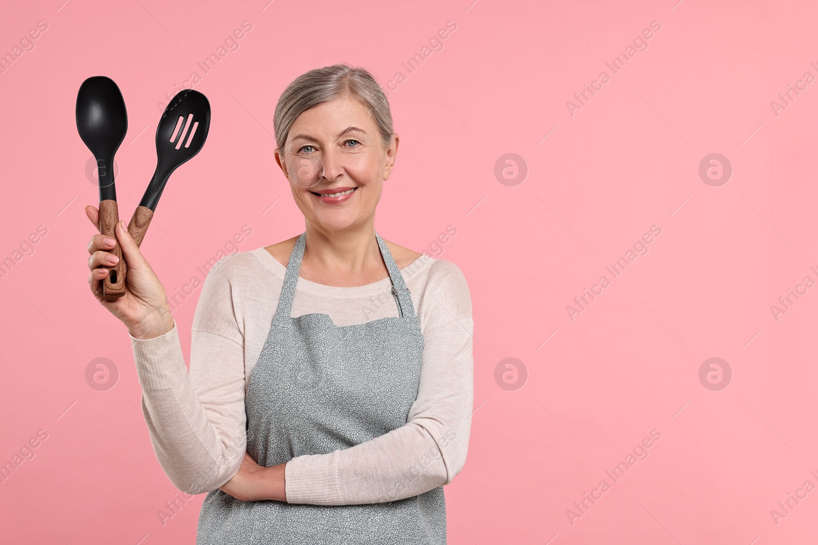 Photo of Happy housewife with spoons on pink background, space for text