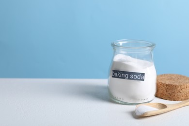 Photo of Baking soda in jar and spoon on white table. Space for text