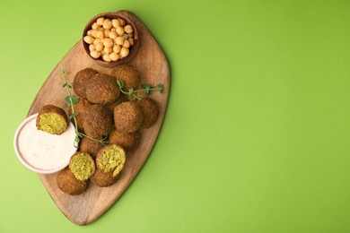 Photo of Delicious falafel balls, chickpeas and sauce on green background, top view. Space for text