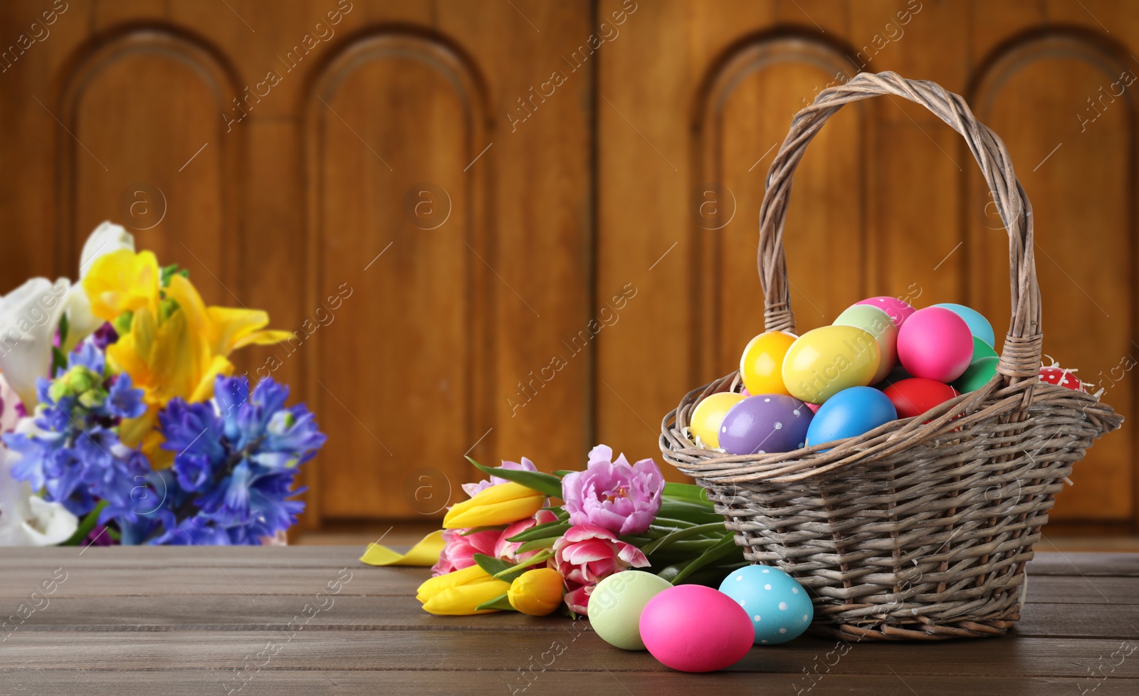 Image of Wicker basket with bright painted Easter eggs on wooden table indoors, space for text 