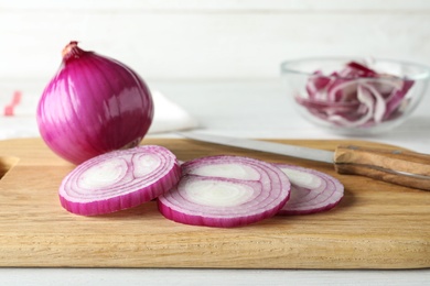 Photo of Wooden board with cut red onion, bulb and knife on white table