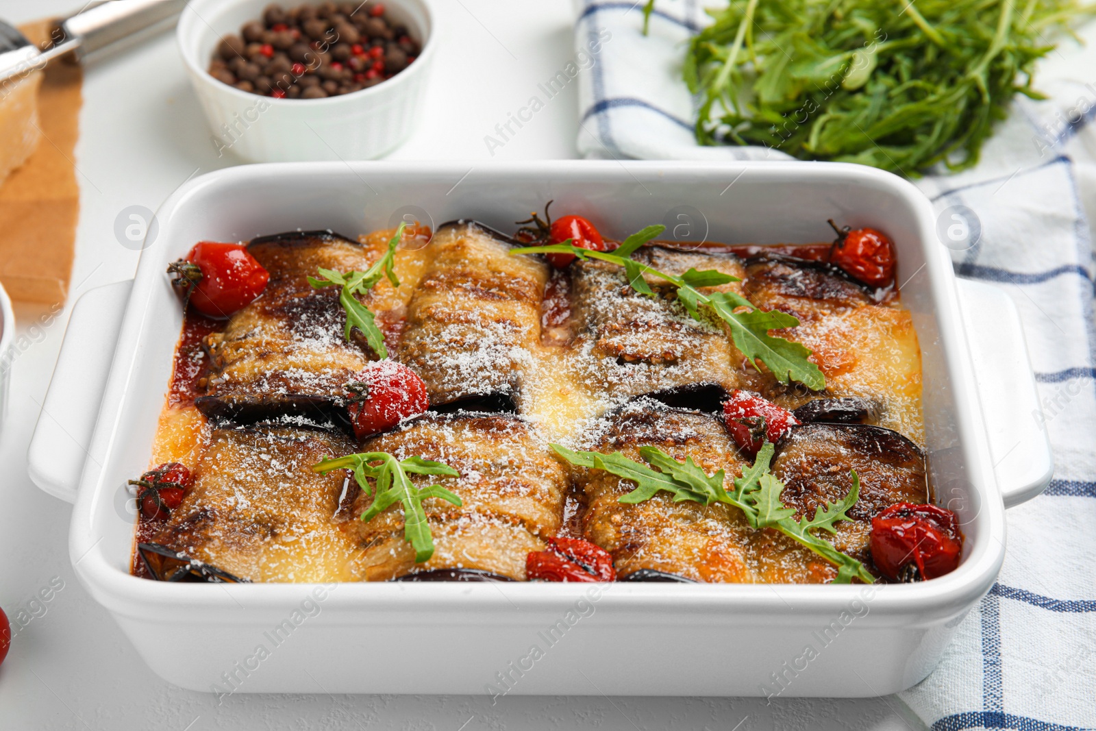 Photo of Tasty eggplant rolls with tomatoes, cheese and arugula in baking dish on white table