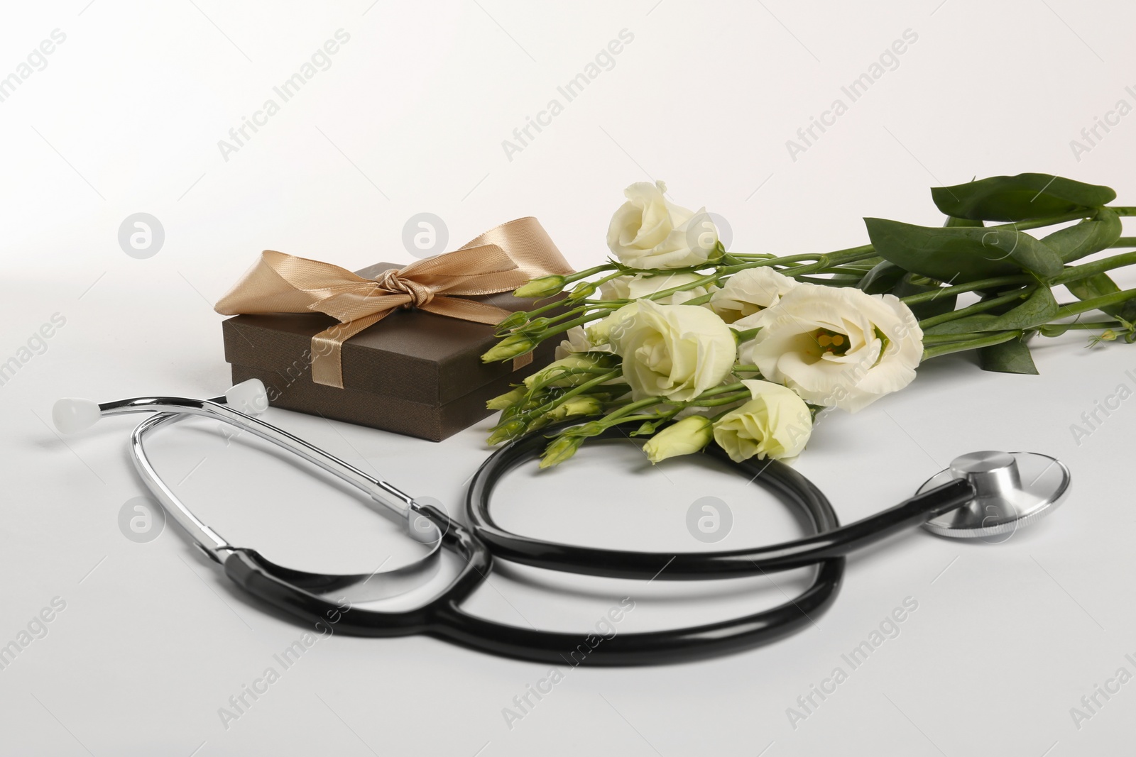 Photo of Stethoscope, gift box and eustoma flowers on white background. Happy Doctor's Day