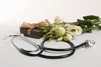 Stethoscope, gift box and eustoma flowers on white background. Happy Doctor's Day