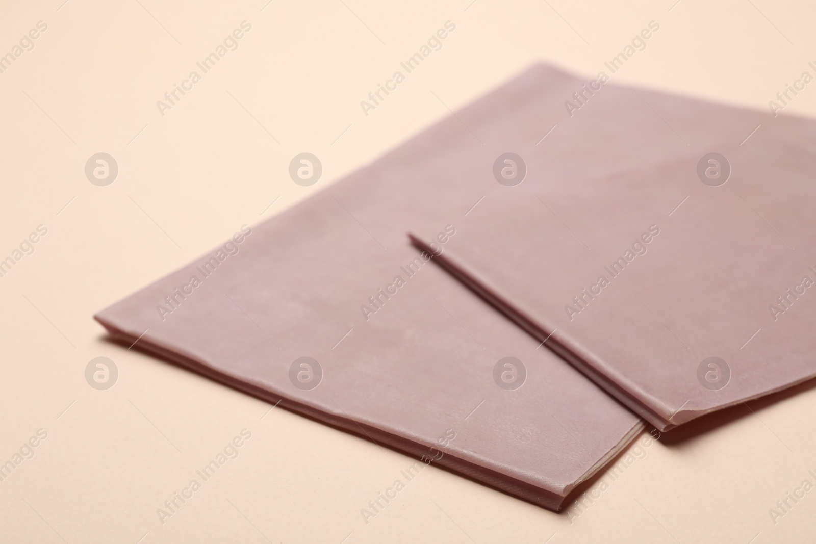 Photo of Pink reusable beeswax food wraps on beige background, closeup