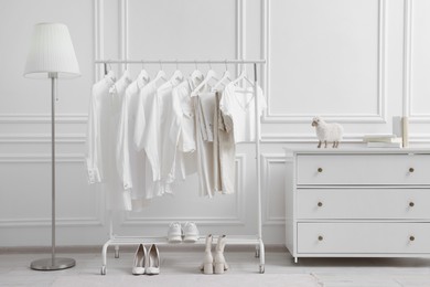 Photo of Rack with different stylish women`s clothes, shoes, lamp and dresser near white wall in room