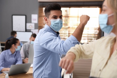 Coworkers with protective masks making elbow bump in office. Informal greeting during COVID-19 pandemic