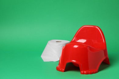 Photo of Red baby potty and toilet paper on green background, space for text