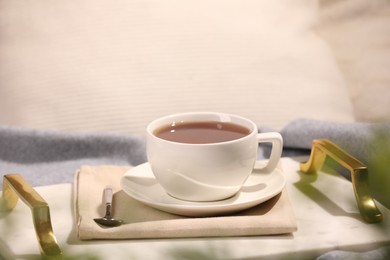 Aromatic tea in cup, saucer and spoon on bed