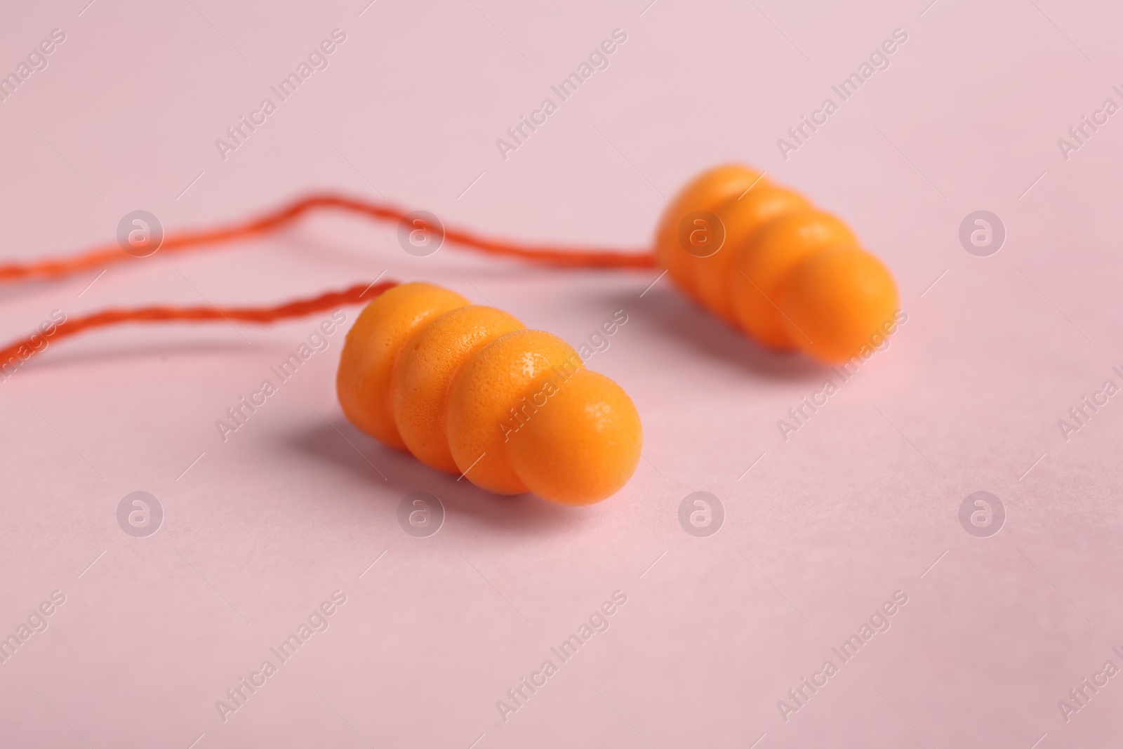 Photo of Pair of orange ear plugs with cord on pink background, closeup