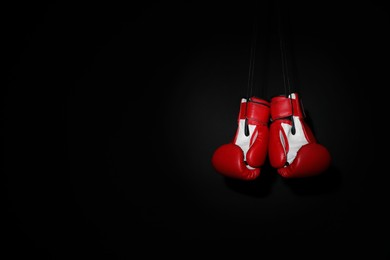Photo of Pair of red boxing gloves hanging on black background, space for text