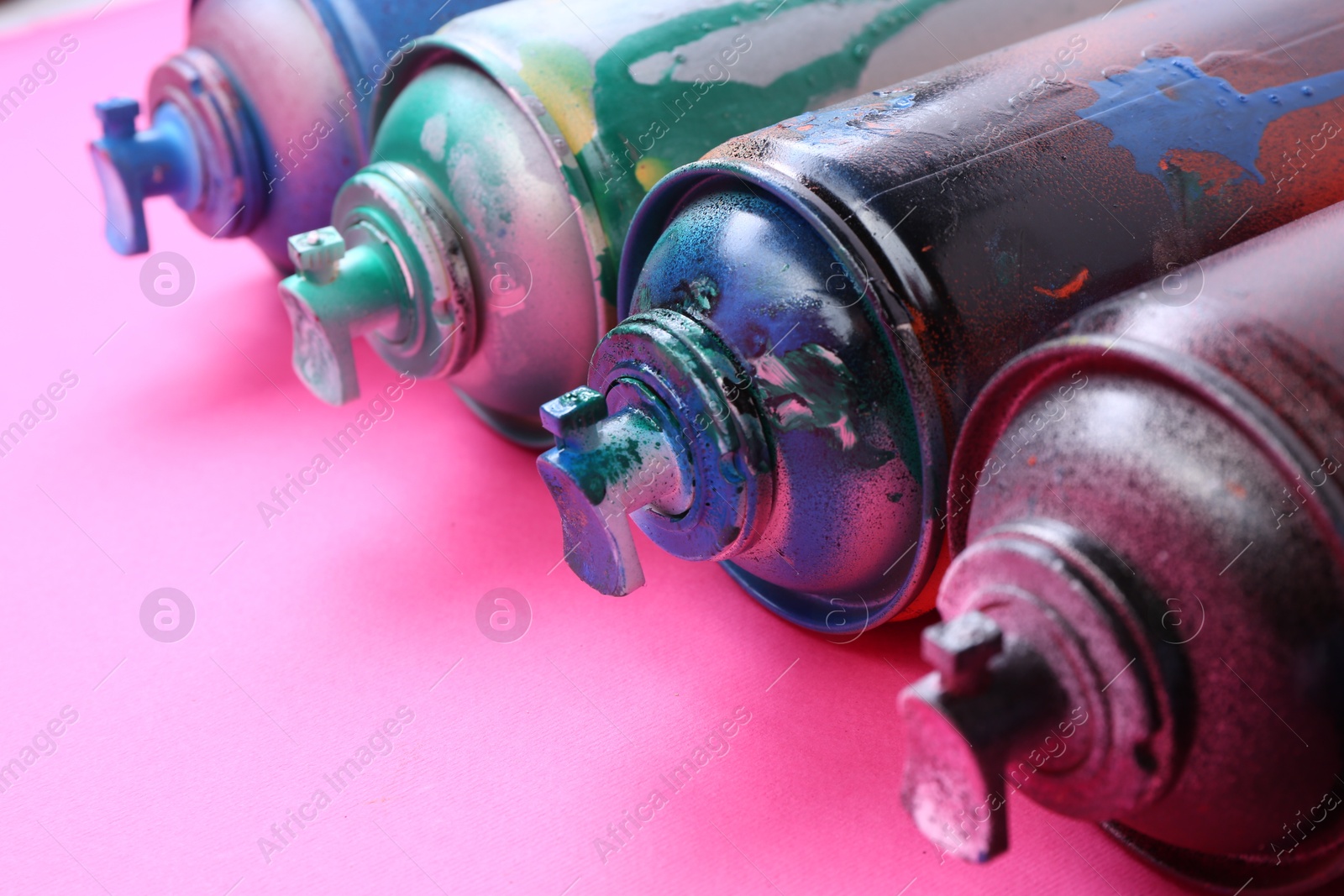 Photo of Many spray paint cans on pink background, closeup