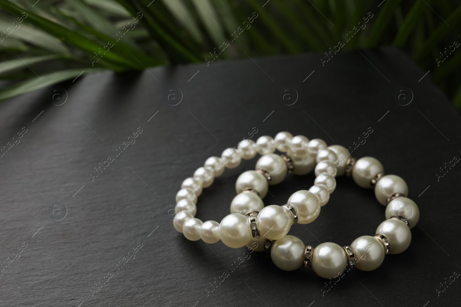 Photo of Elegant pearl bracelets on black table, closeup. Space for text