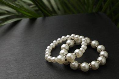 Elegant pearl bracelets on black table, closeup. Space for text