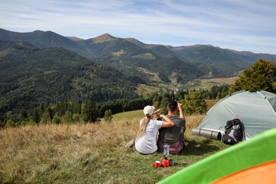 Photo of Couple enjoying mountain landscape near camping tent, back view