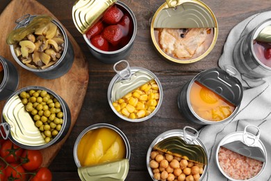 Open tin cans with different products on wooden table, flat lay