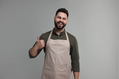 Photo of Smiling man in kitchen apron showing thumb up on grey background. Mockup for design