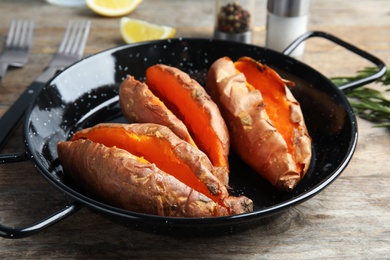 Dish with baked sweet potatoes on wooden table, closeup