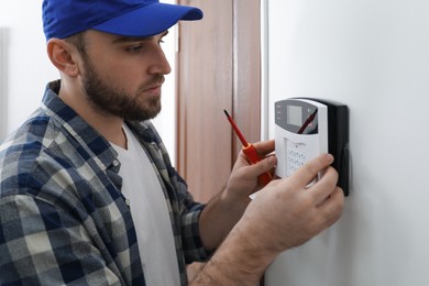 Man installing home security system on white wall in room